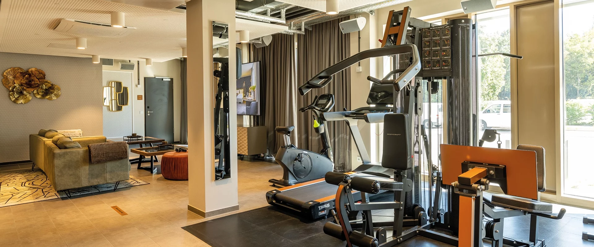 Fitnessraum eines MASEVEN Hotels mit modernen Fitnessgeräten und Fenstern